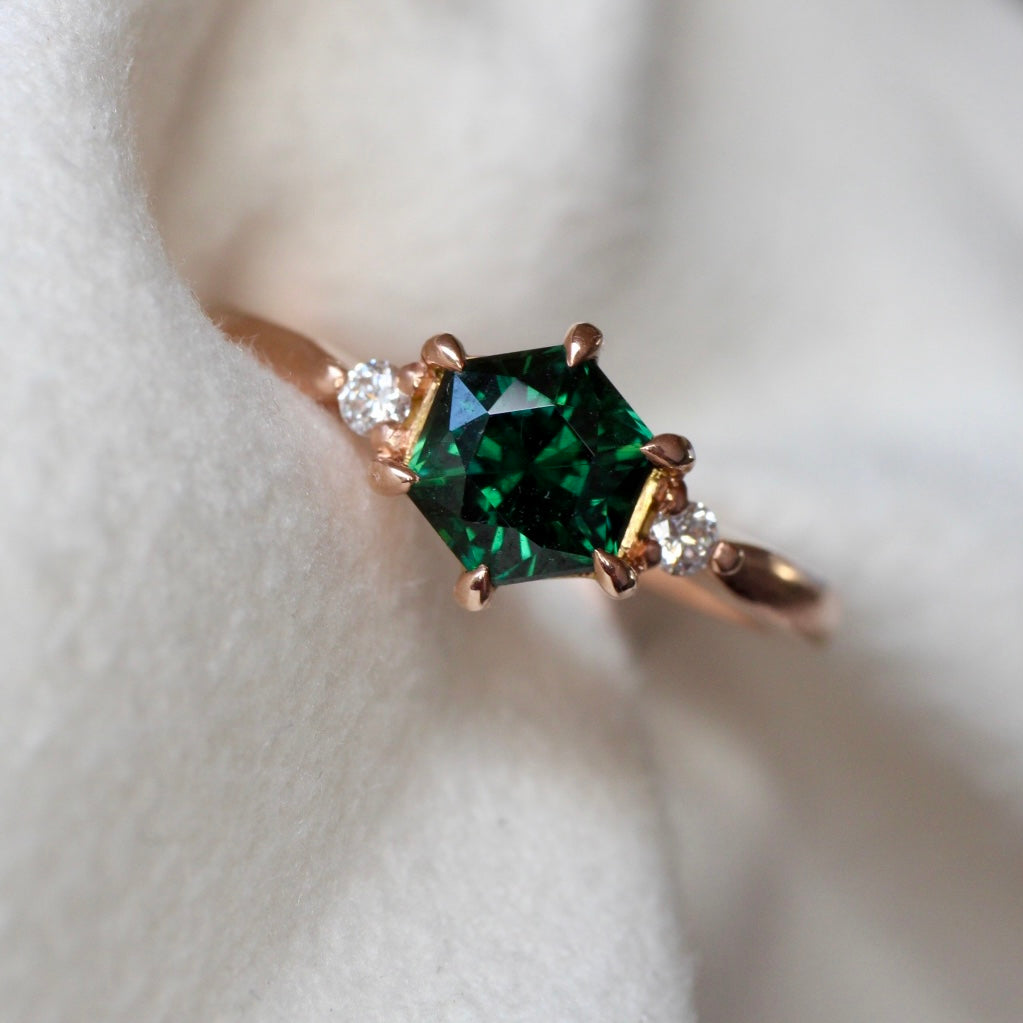 Vibrant Australian Green hexagonal Cut Sapphire & Diamond Helena ring. The sapphire is set with six eagle claws. The stone is beautifully complimented by two 2mm 0.03pt Round Brilliant cut diamonds total diamond weight 0.06pts and is set in 14ct Rose gold.  The Sapphire measures 6.8mm & is 1.45cts   The ring is size O (can be sized J-R)   Made with recycled metal in Sydney   Ethically sourced Gemstones