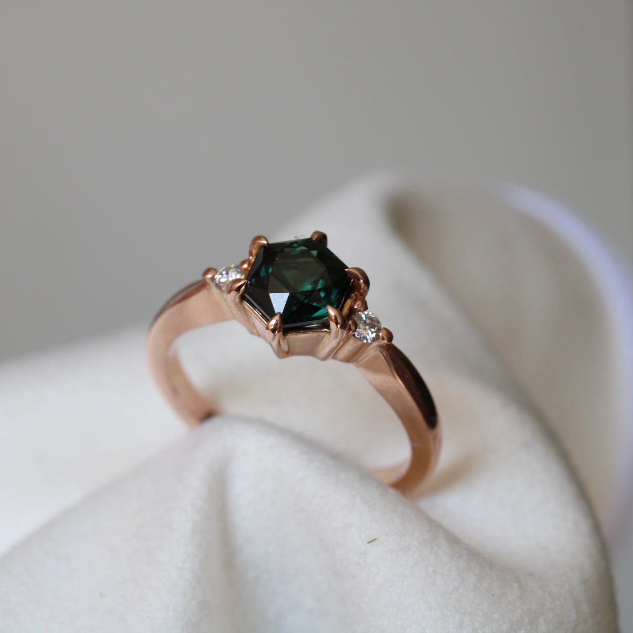 Vibrant Australian Green hexagonal Cut Sapphire & Diamond Helena ring. The sapphire is set with six eagle claws. The stone is beautifully complimented by two 2mm 0.03pt Round Brilliant cut diamonds total diamond weight 0.06pts and is set in 14ct Rose gold. The Sapphire measures 6.8mm & is 1.45cts The ring is size O (can be sized J-R) Made with recycled metal in Sydney Ethically sourced Gemstones