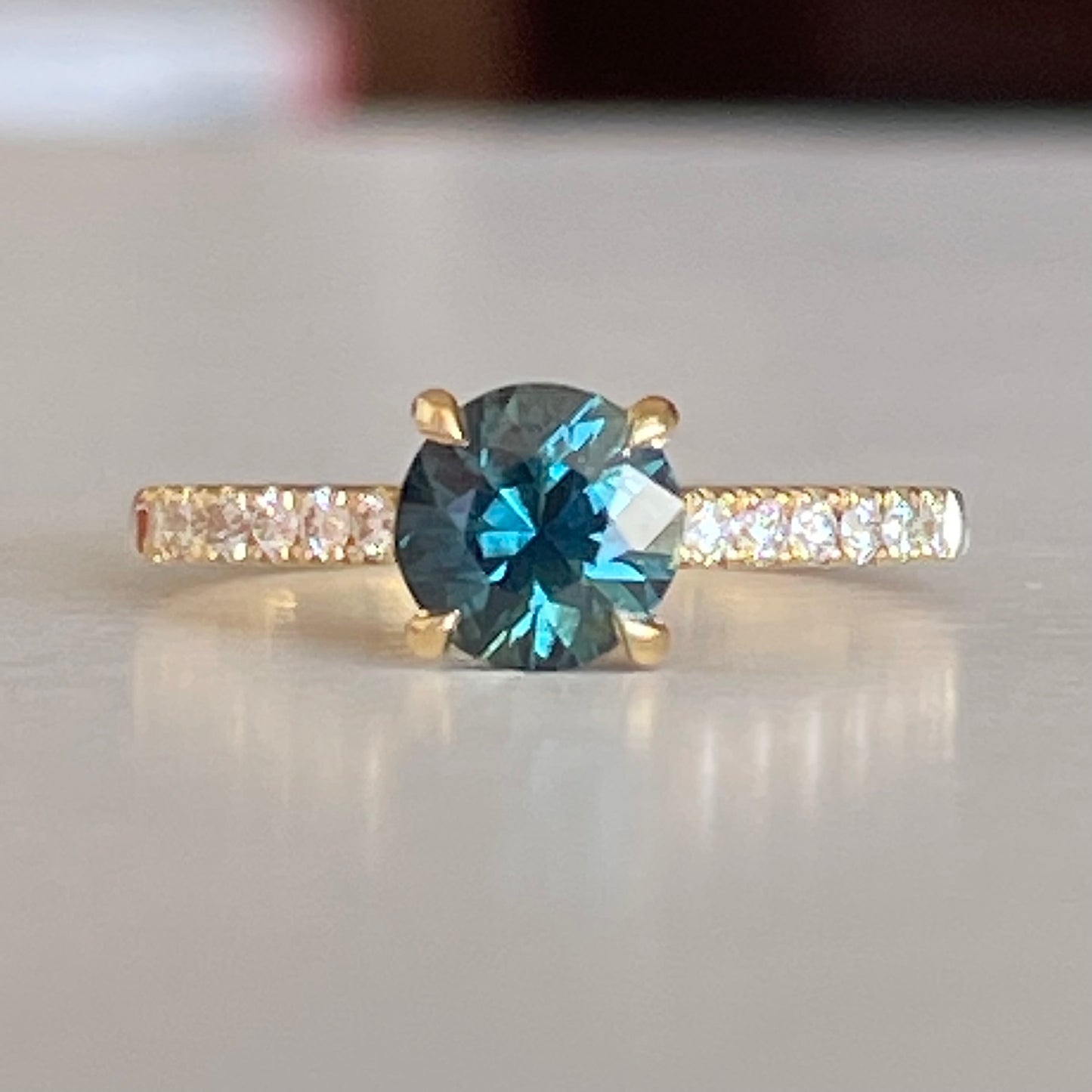 A Blue/Green Australian Parti Sapphire from Rubyvale in QLD & is set with four claws. The stone is beautifully complimented by 12 x Round Brilliant cut total diamond weight 0.18pts and is set in 18ct Yellow gold. The Sapphire measures 6.4mm and is 1.16cts Available in Size M Made with recycled metal in Sydney Ethically sourced Gemstones