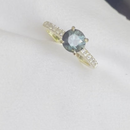 A Blue/Green Australian Parti Sapphire from Rubyvale in QLD & is set with four claws. The stone is beautifully complimented by 12 x Round Brilliant cut total diamond weight 0.18pts and is set in 18ct Yellow gold.  The Sapphire measures 6.4mm and is 1.16cts   Available in Size M  Made with recycled metal in Sydney   Ethically sourced Gemstones 