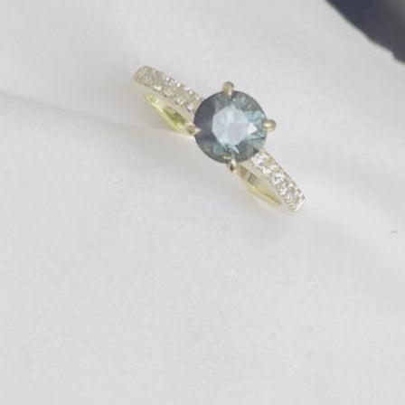 A Blue/Green Australian Parti Sapphire from Rubyvale in QLD & is set with four claws. The stone is beautifully complimented by 12 x Round Brilliant cut total diamond weight 0.18pts and is set in 18ct Yellow gold.  The Sapphire measures 6.4mm and is 1.16cts   Available in Size M  Made with recycled metal in Sydney   Ethically sourced Gemstones 