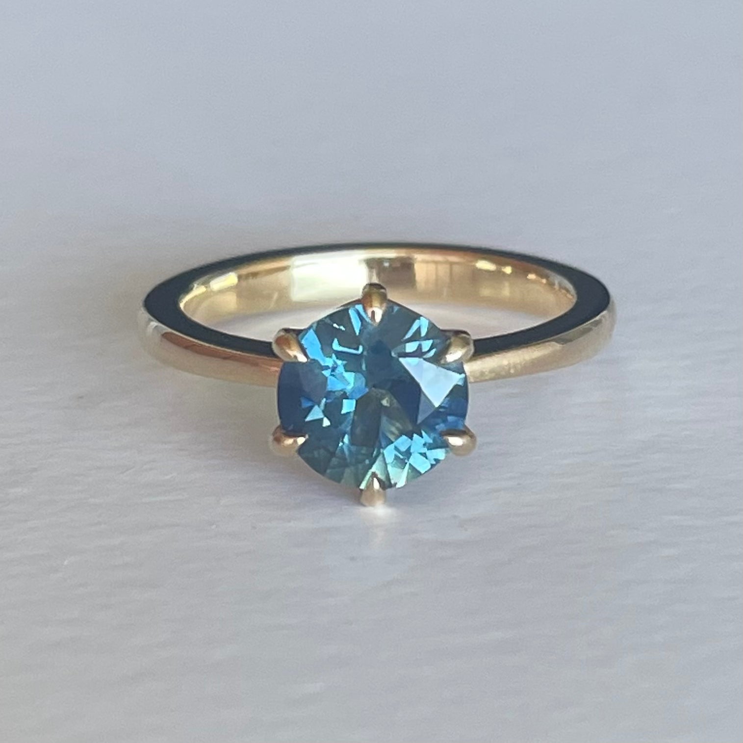 This 14ct Yellow Gold Solitare Chloe Sapphire Ring featuring a Light Blue Australian Parti Sapphire and is set with 6 claws. The band is pinched at the top, the claws are set in an eagle claw shape   The Sapphire measures 7.5mm & is 1.69ct in weight  This ring is a size L (it can be resized I-Q)   Made with recycled metal in Sydney   Ethically sourced Gemstones 