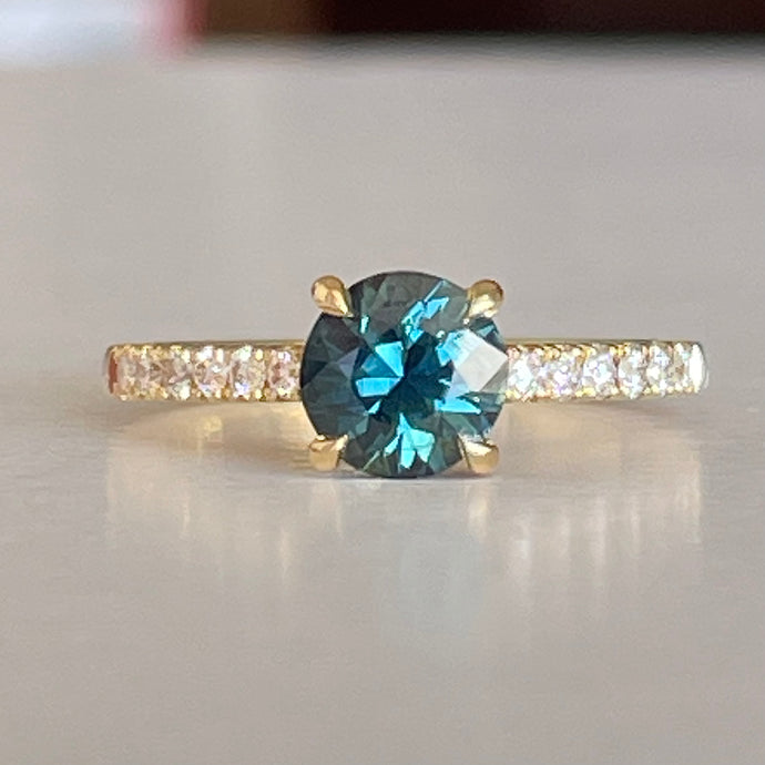 A Blue/Green Australian Parti Sapphire from Rubyvale in QLD & is set with four claws. The stone is beautifully complimented by 12 x Round Brilliant cut total diamond weight 0.18pts and is set in 18ct Yellow gold.  The Sapphire measures 6.4mm and is 1.16cts   Available in Size M  Made with recycled metal in Sydney   Ethically sourced Gemstones 