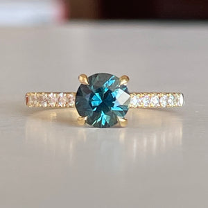 A Blue/Green Australian Parti Sapphire from Rubyvale in QLD & is set with four claws. The stone is beautifully complimented by 12 x Round Brilliant cut total diamond weight 0.18pts and is set in 18ct Yellow gold.  The Sapphire measures 6.4mm and is 1.16cts   Available in Size M  Made with recycled metal in Sydney   Ethically sourced Gemstones 